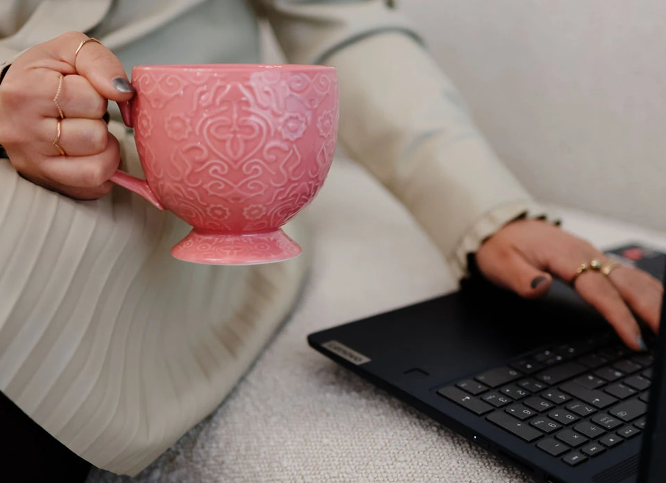 Caroline Burnell, Counsellor, holding a large mug in one hand, and typing on a laptop with the other hand.
