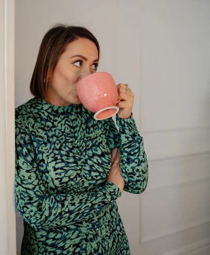 Caroline Burnell, Counsellor, gently leaning against a wall, drinking from a large mug, looking away from the camera in thought.